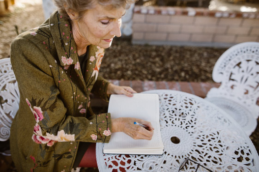 Elderly woman sitting outdoors and writing in a notebook