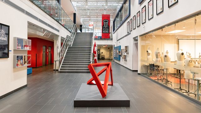 The interior of the LaSalle College Vancouver building, showing a red sculpture in the hallway and a brightly lit classroom containing mannequins for design classes.