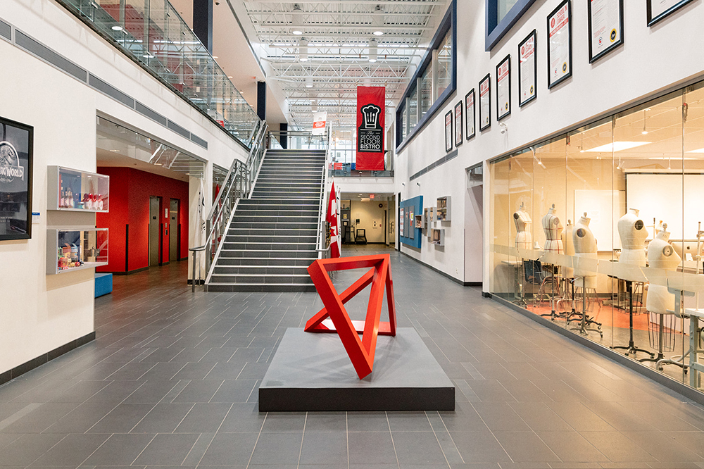 The interior of the LaSalle College Vancouver building, showing a red sculpture in the hallway and a brightly lit classroom containing mannequins for design classes.
