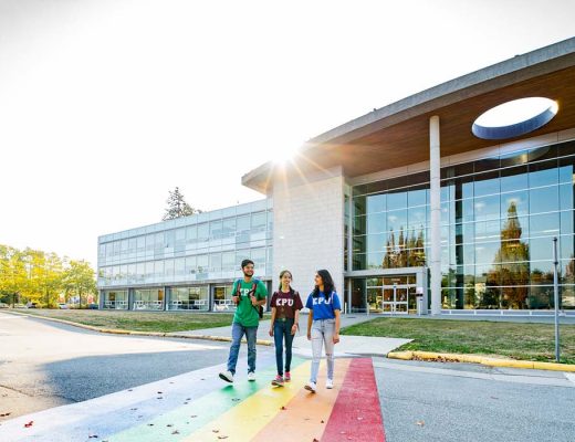 Three students cross the street outside one of Kwantlen Polytechnic University's campuses on a sunny day.