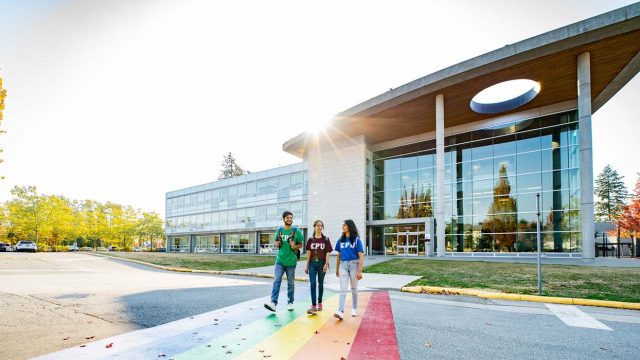 Three students cross the street outside one of Kwantlen Polytechnic University's campuses on a sunny day.