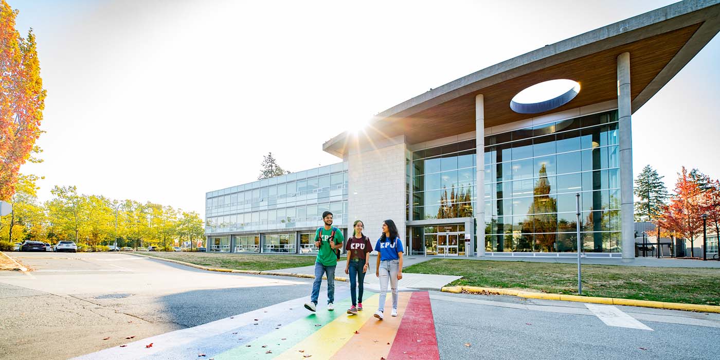 Three students cross the street outside one of Kwantlen Polytechnic University's campuses on a sunny day.