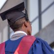 An African male graduate wearing a blue and red graduation gown and black graduation cap.