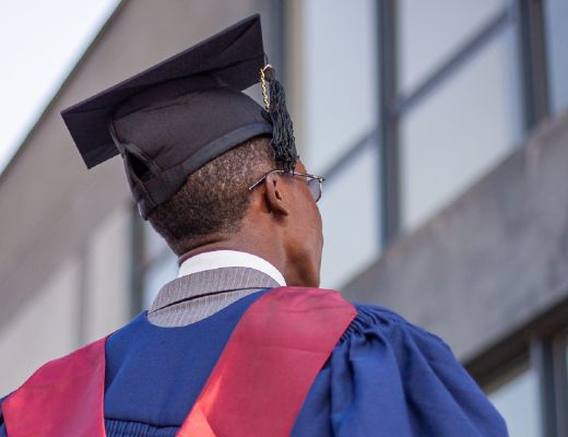 An African male graduate wearing a blue and red graduation gown and black graduation cap.