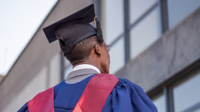 An African male graduate wearing a blue and red graduation gown and black graduation cap.