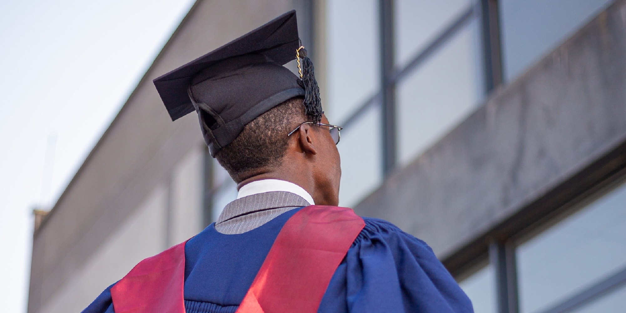 An African male graduate wearing a blue and red graduation gown and black graduation cap.