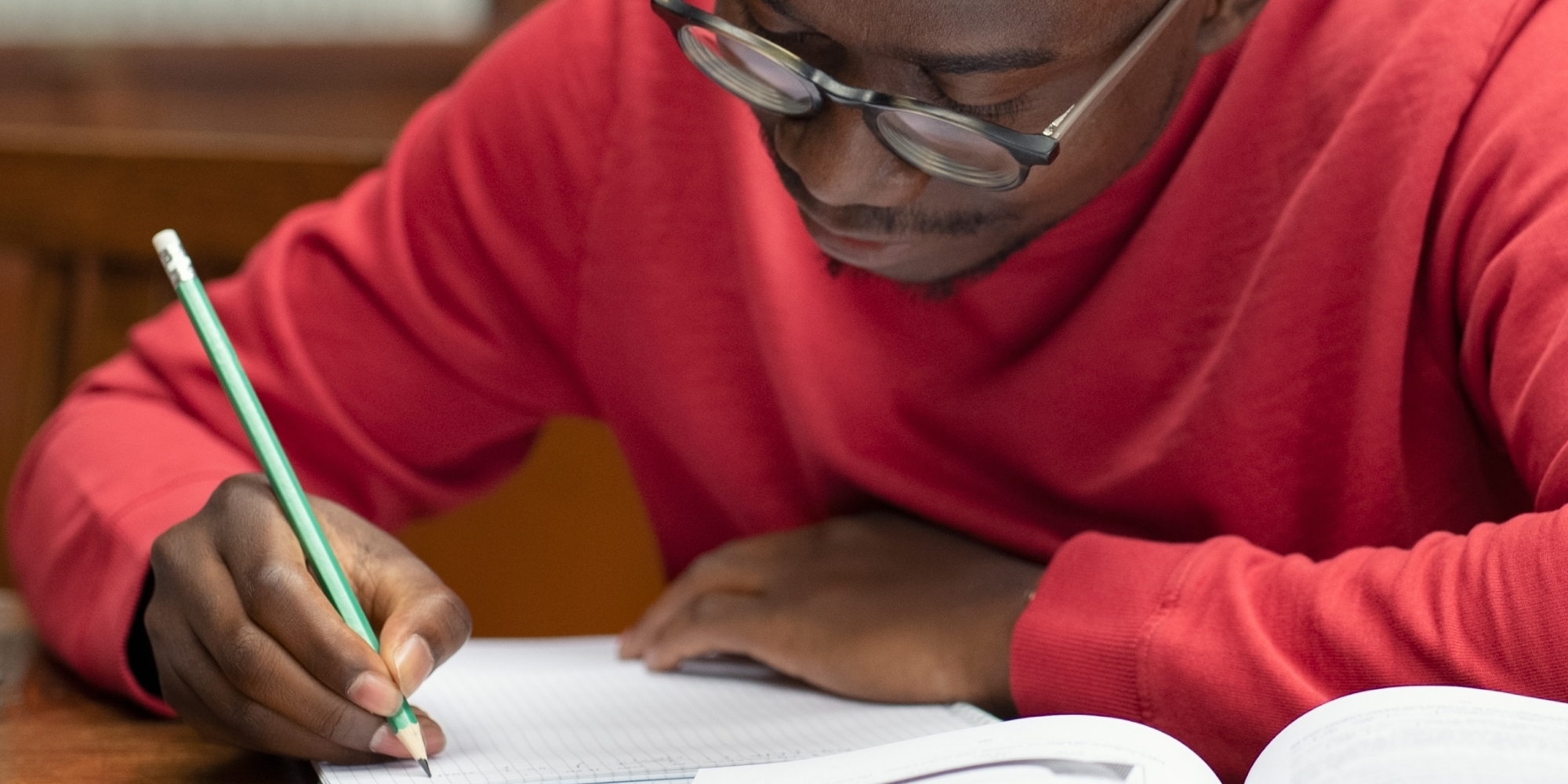 A young African male university student wearing spectacles studying in a library. 