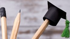 Three pencils in a pencil holder with a tiny graduate hat on one of the pencils.