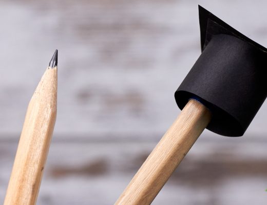 Three pencils in a pencil holder with a tiny graduate hat on one of the pencils.