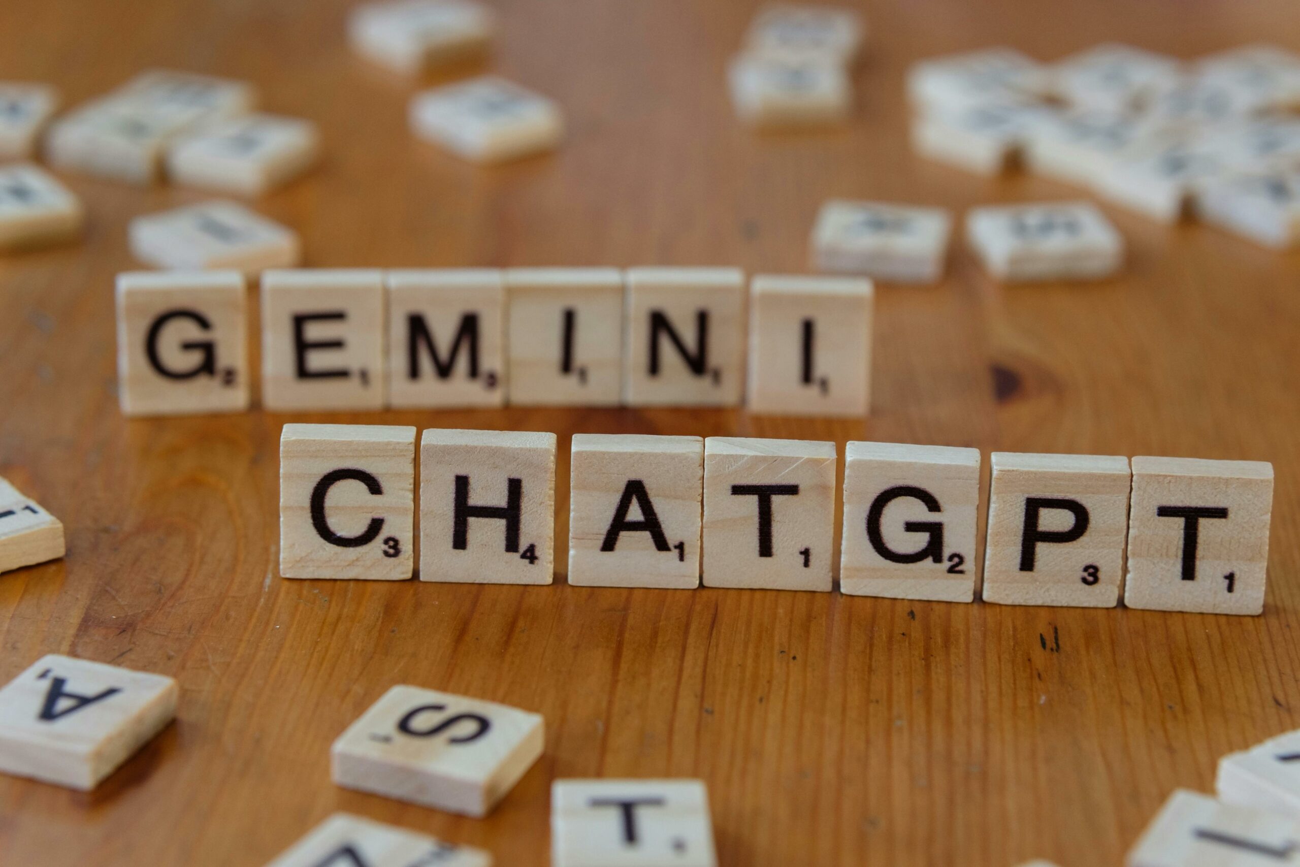 Wooden Scrabble tiles spell "GEMINI" above "CHATGPT" on a wooden surface. Scattered tiles are in the background, creating a playful, creative vibe.
